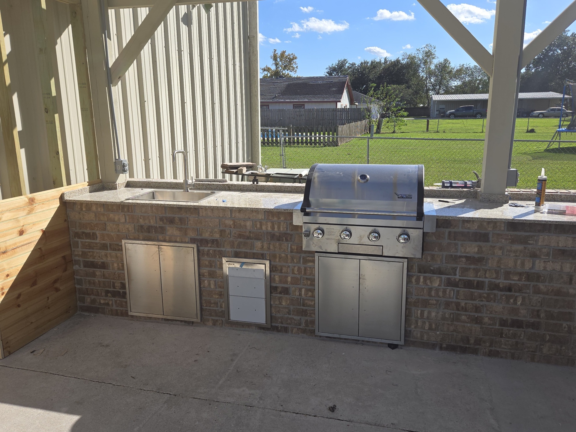 Finished outdoor kitchen with built-in grill, sink, and storage cabinets
