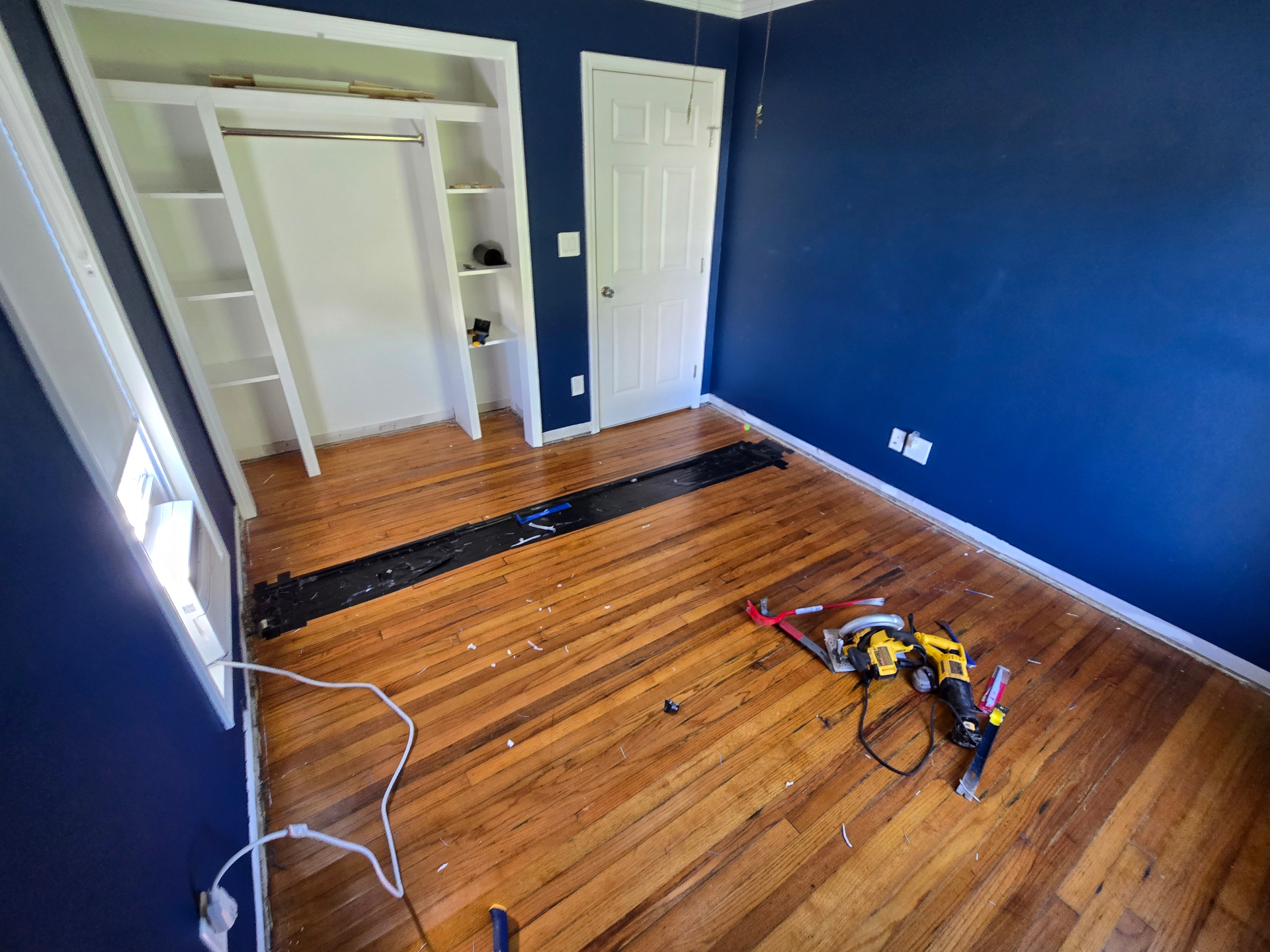 Bedroom before repair with damaged hardwood flooring and tools staged in the room