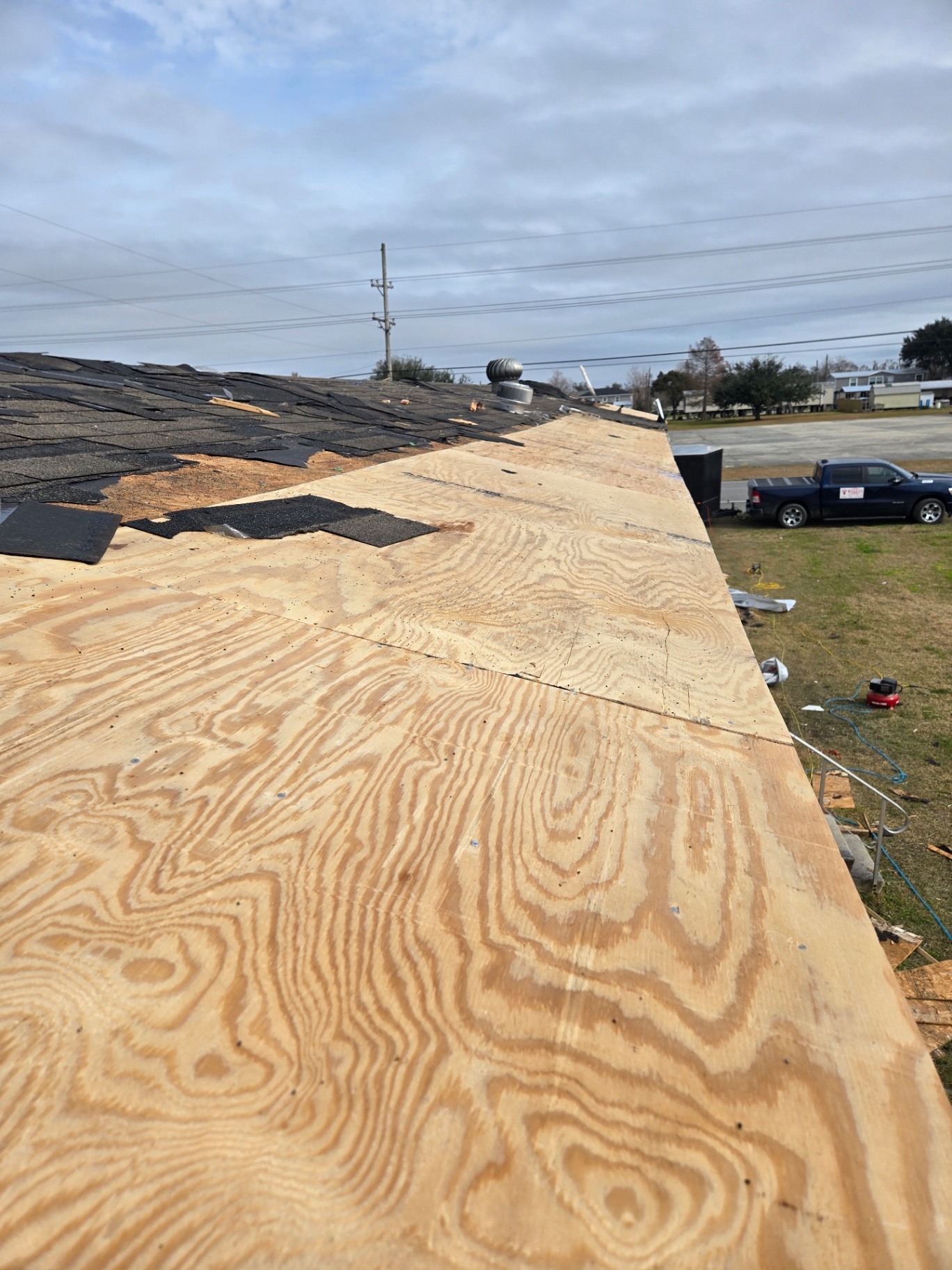 Old asphalt shingles being torn off with new plywood decking exposed along the roof edge