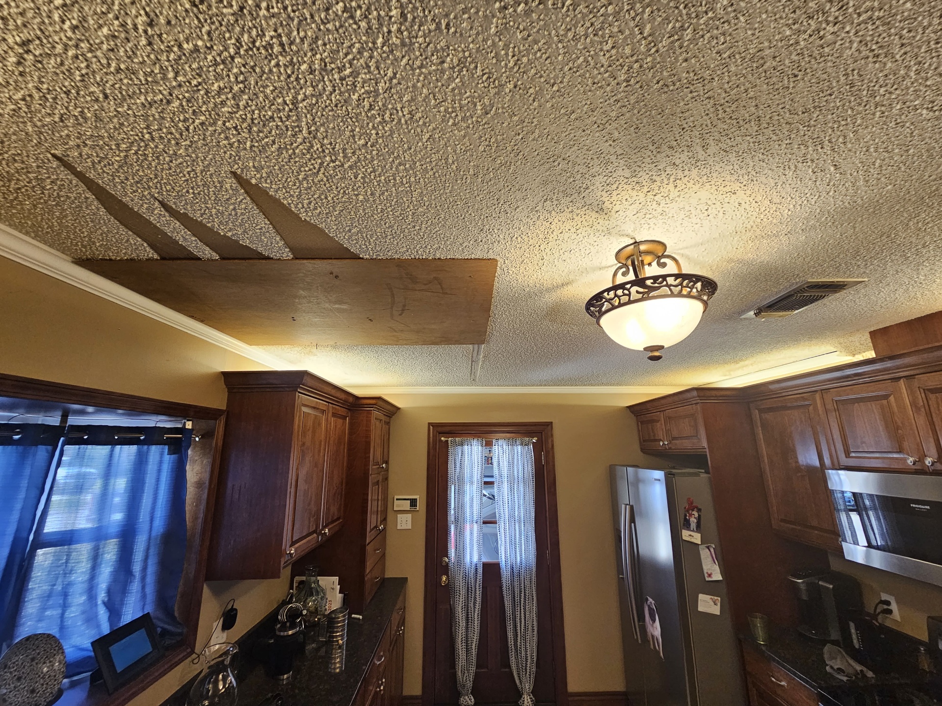 Original popcorn ceiling in the kitchen with patched wood section before repair