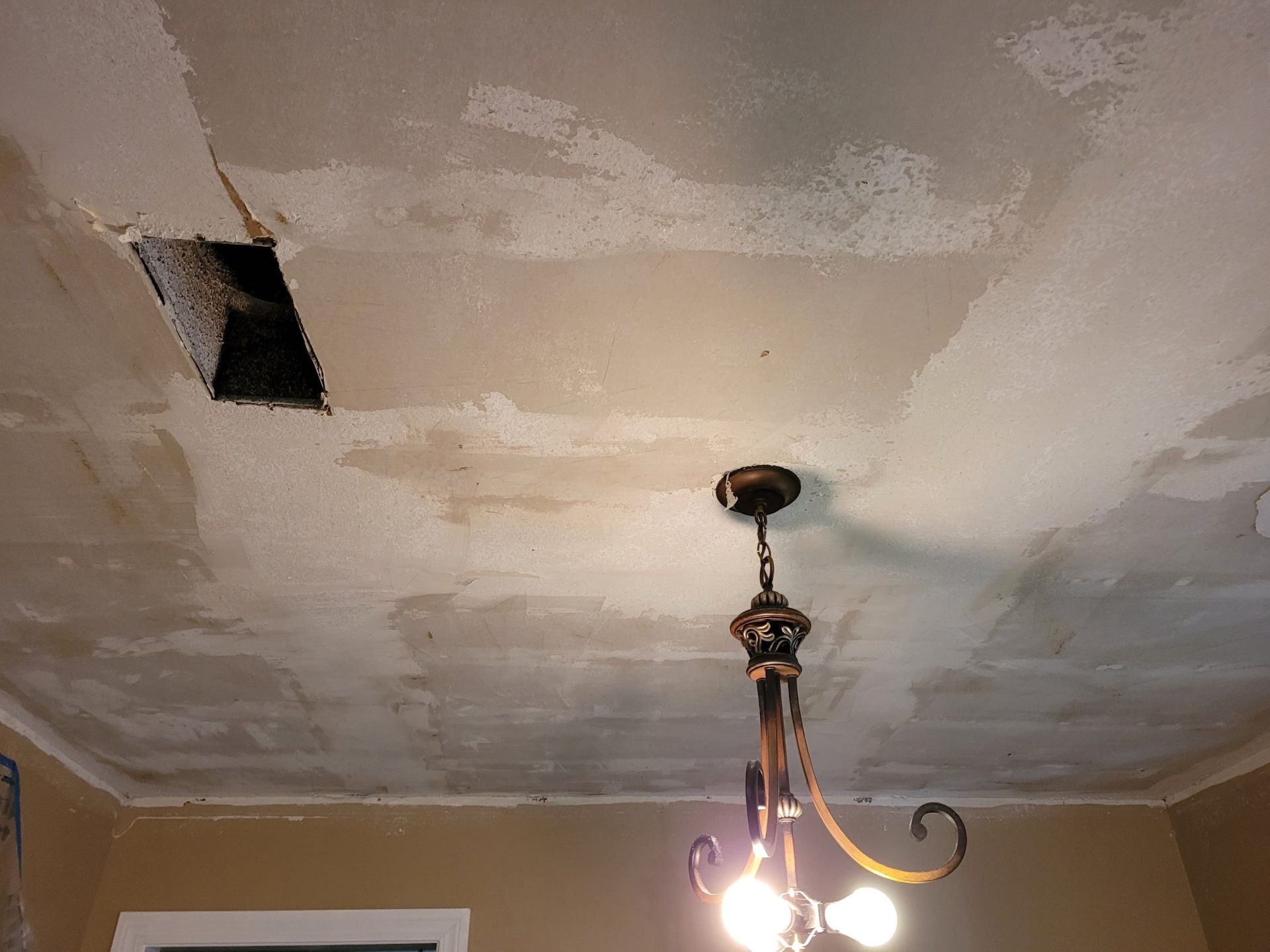 Damaged ceiling with vent hole and peeling popcorn texture before repair