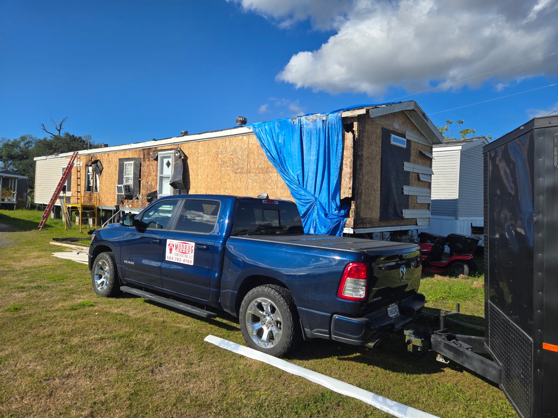 Wide view of the mobile home during exterior rebuild with damaged section tarped